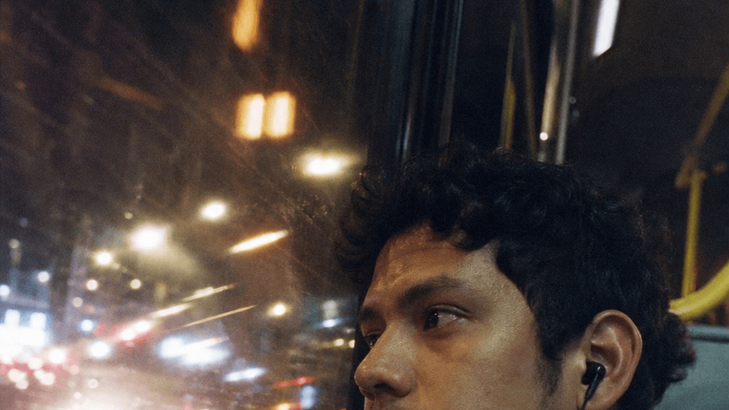 A young man rides a city bus at night, the lit street motion-streaked across the window — made with GPT Image 2 Medium.